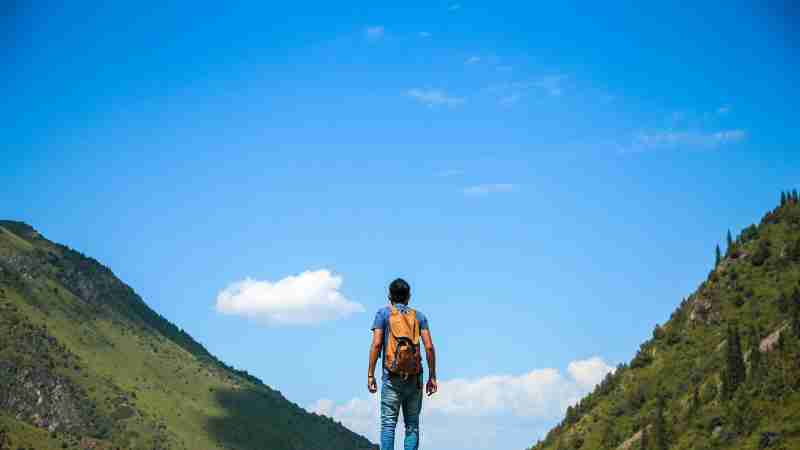 A solo backpacker standing on a rock, admiring the mountain view under a bright blue sky., tags: arcevia - pexel